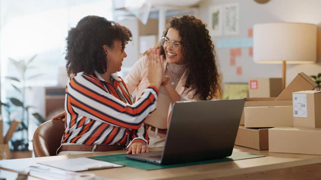 Duas mulheres comemorando vendas online em frente a um notebook, simbolizando sucesso em marketplaces para mulheres empreendedoras.