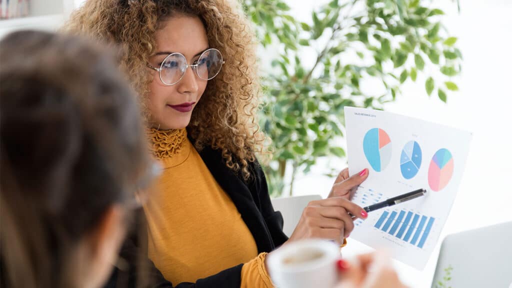 Mulher analisando gráficos durante reunião, representando a importância da pesquisa de mercado para pequenos negócios na tomada de decisões estratégicas.