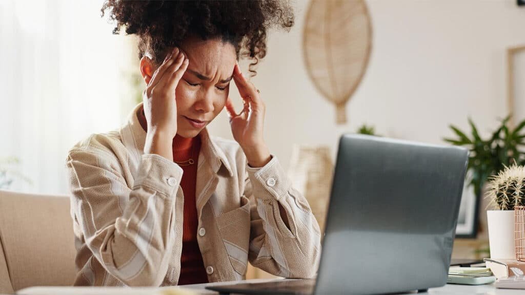 Mulher empreendedora preocupada diante do computador, representando os efeitos da Síndrome da Impostora no trabalho