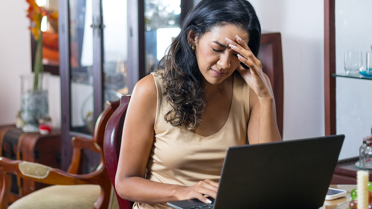 Mulher empreendedora à frente do laptop, com expressão de cansaço e mão na testa, representando os impactos do burnout no empreendedorismo feminino.