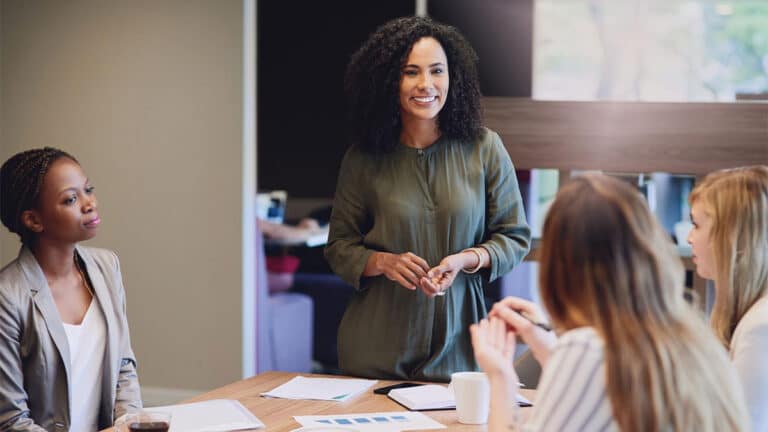 Mulher negra liderando reunião em ambiente de trabalho, simbolizando liderança feminina e gestão humanizada﻿, com foco na colaboração, comunicação empática e inclusão entre a equipe presente.