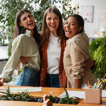 Três mulheres empreendedores abraçadas e felizes em escritório representando a relação entre empreendedorismo e empoderamento feminino